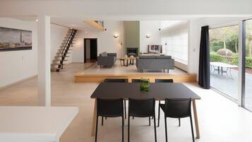 Un intérieur moderne comprenant un coin repas, des canapés, un escalier et une grande fenêtre.
