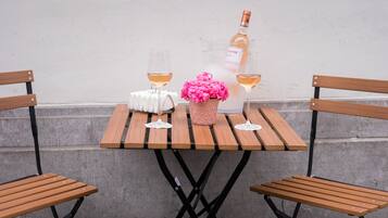 A wooden table with two glasses of white wine, a bottle of wine, and a pink flower arrangement.