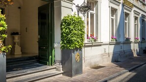 A hotel entrance with a green awning, a large potted plant, and a staircase leading to the entrance. - Relais & Chateaux Hotel Heritage (Bruges)