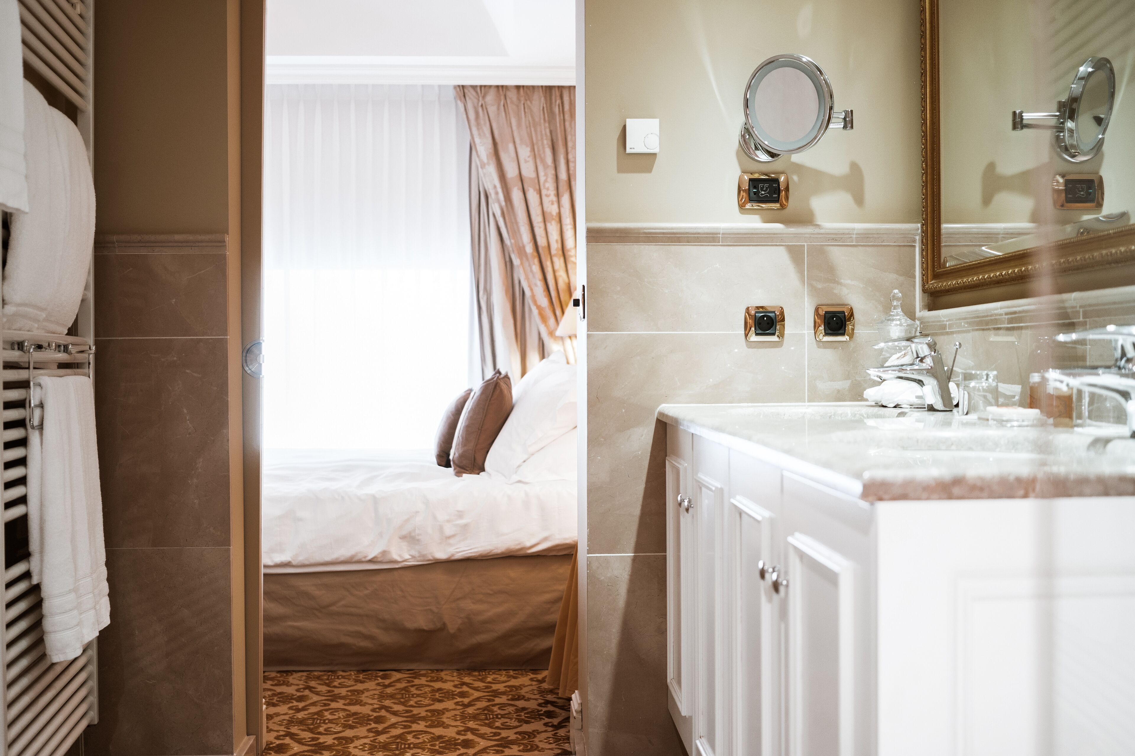 A hotel room with a bed, a bathroom with a sink and mirror, and a window with curtains.