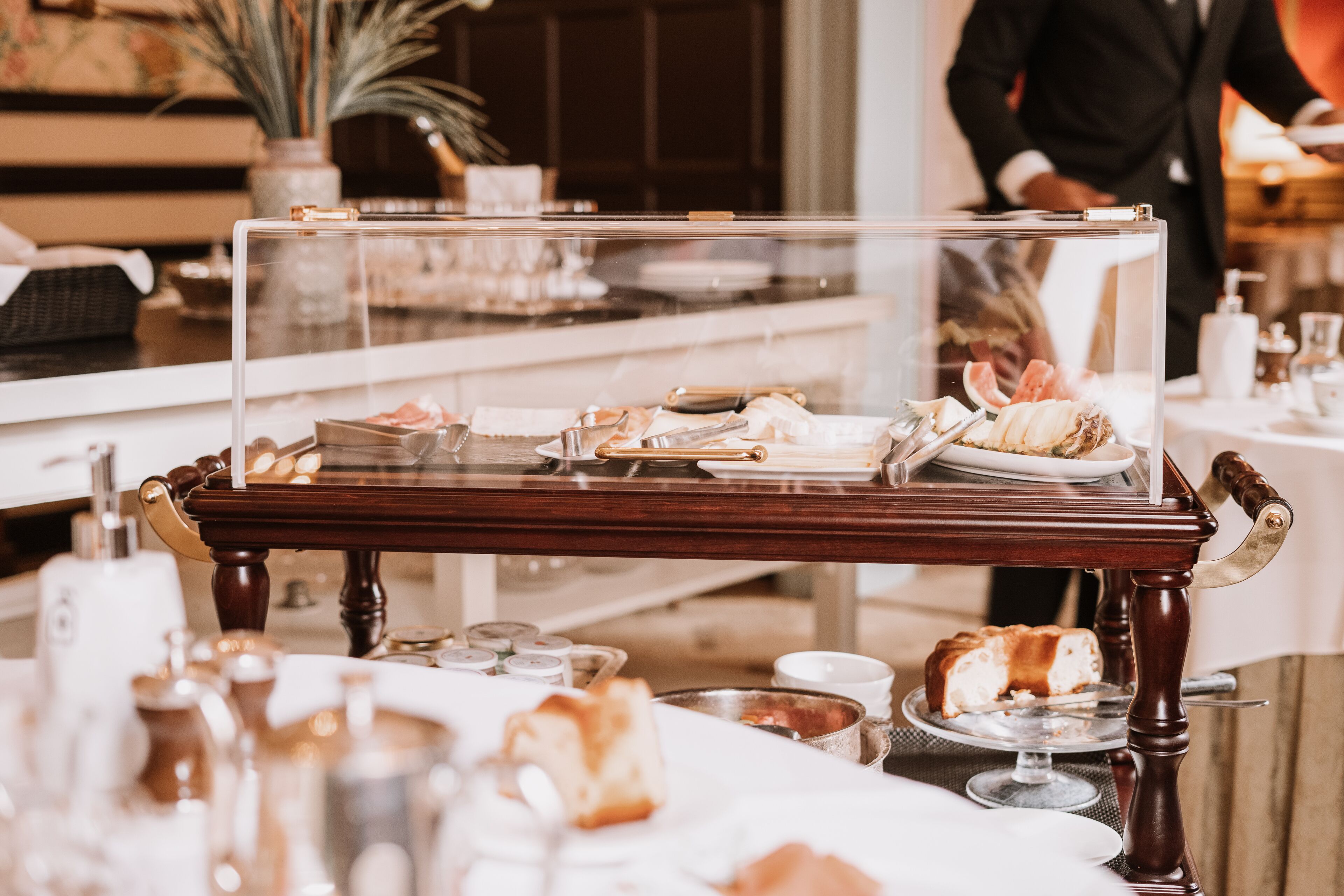 A dining area with a clear display case containing pastries and a wooden table with various dishes and utensils.