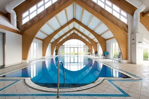 Une piscine intérieure dotée d’un haut plafond, de poutres en bois et d’un sol carrelé.