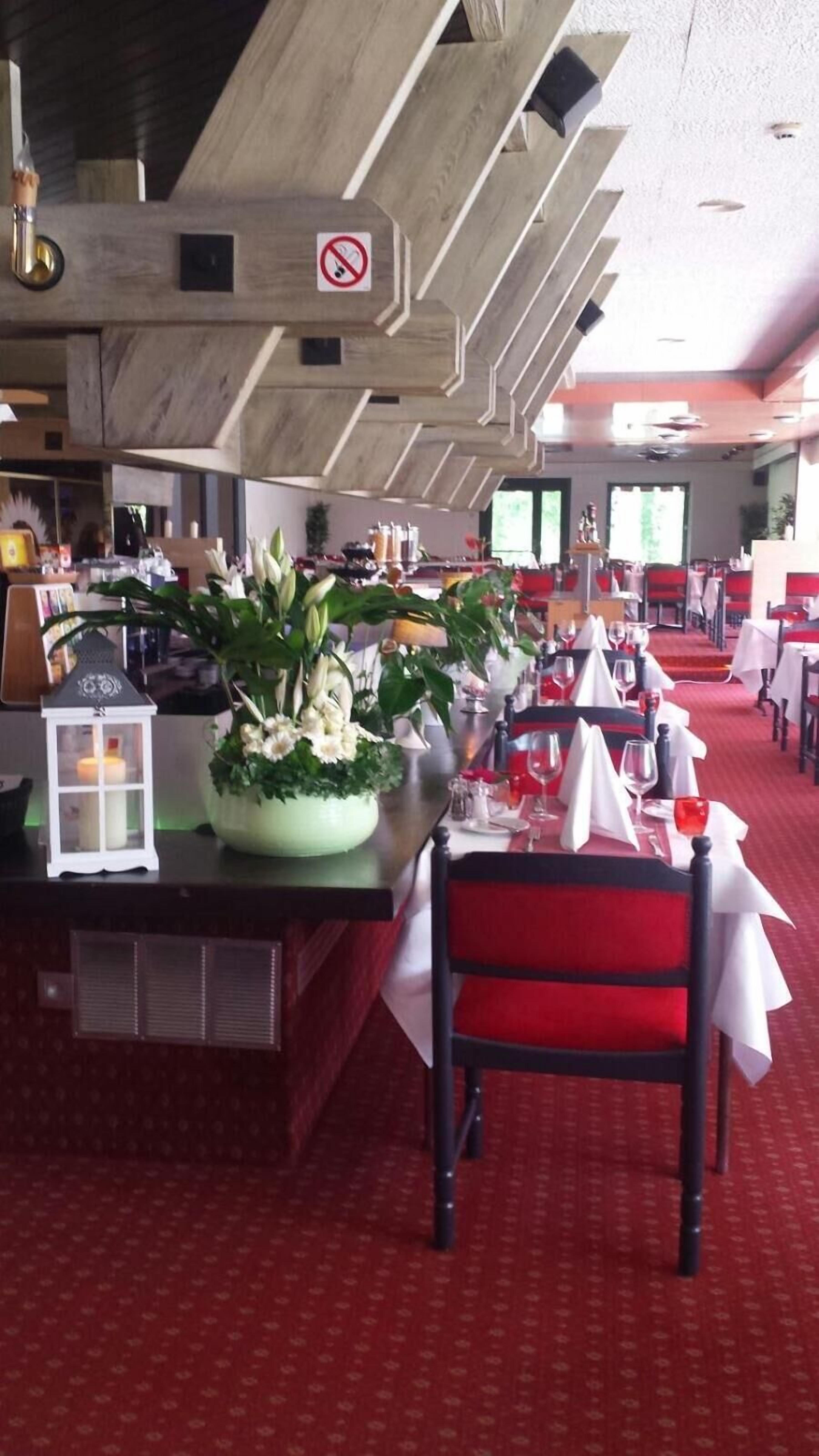Un restaurant avec des tables recouvertes de moquette rouge, des nappes blanches et un panneau indiquant qu'il est interdit de fumer.