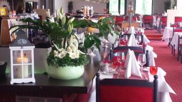 Een restaurant met rode tapijten onder de tafels, witte tafelkleden en een rookvrij bord.