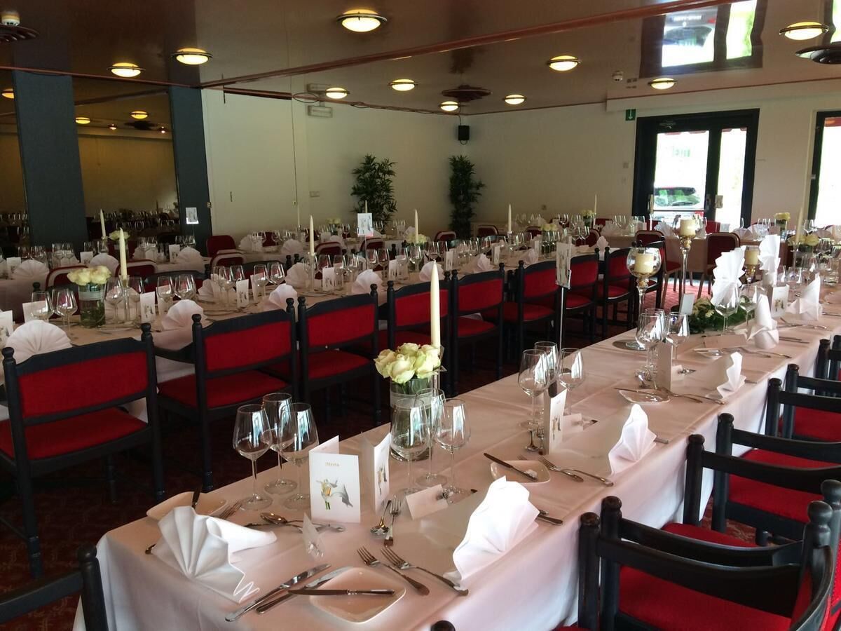 Un salón de banquetes con filas de mesas dispuestas para un evento formal, cada una con manteles blancos, sillas rojas y centros de mesa con velas.