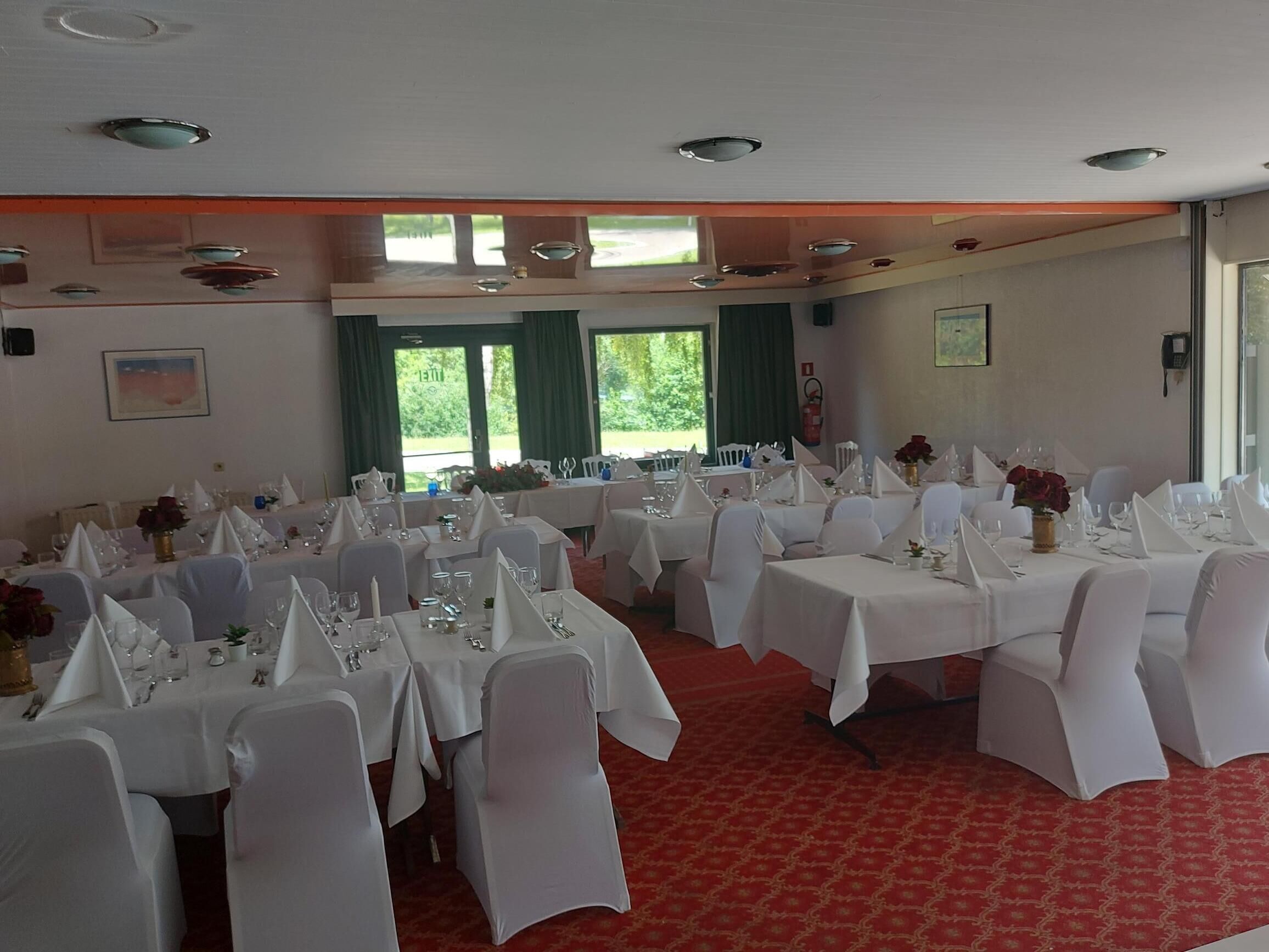 Une salle de banquet avec de nombreuses tables rondes, des nappes blanches et des chaises recouvertes d’un tissu blanc.