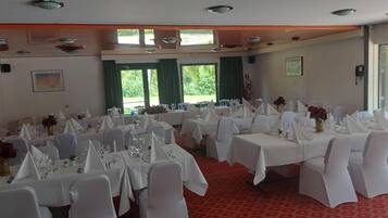 Een feestzaal met meerdere ronde tafels, witte tafelkleden en stoelen bekleed met witte stof.