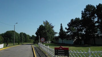 A road with a speed limit sign, a directional sign for Reception, Restaurant, and Fournisseurs, and a white fence.