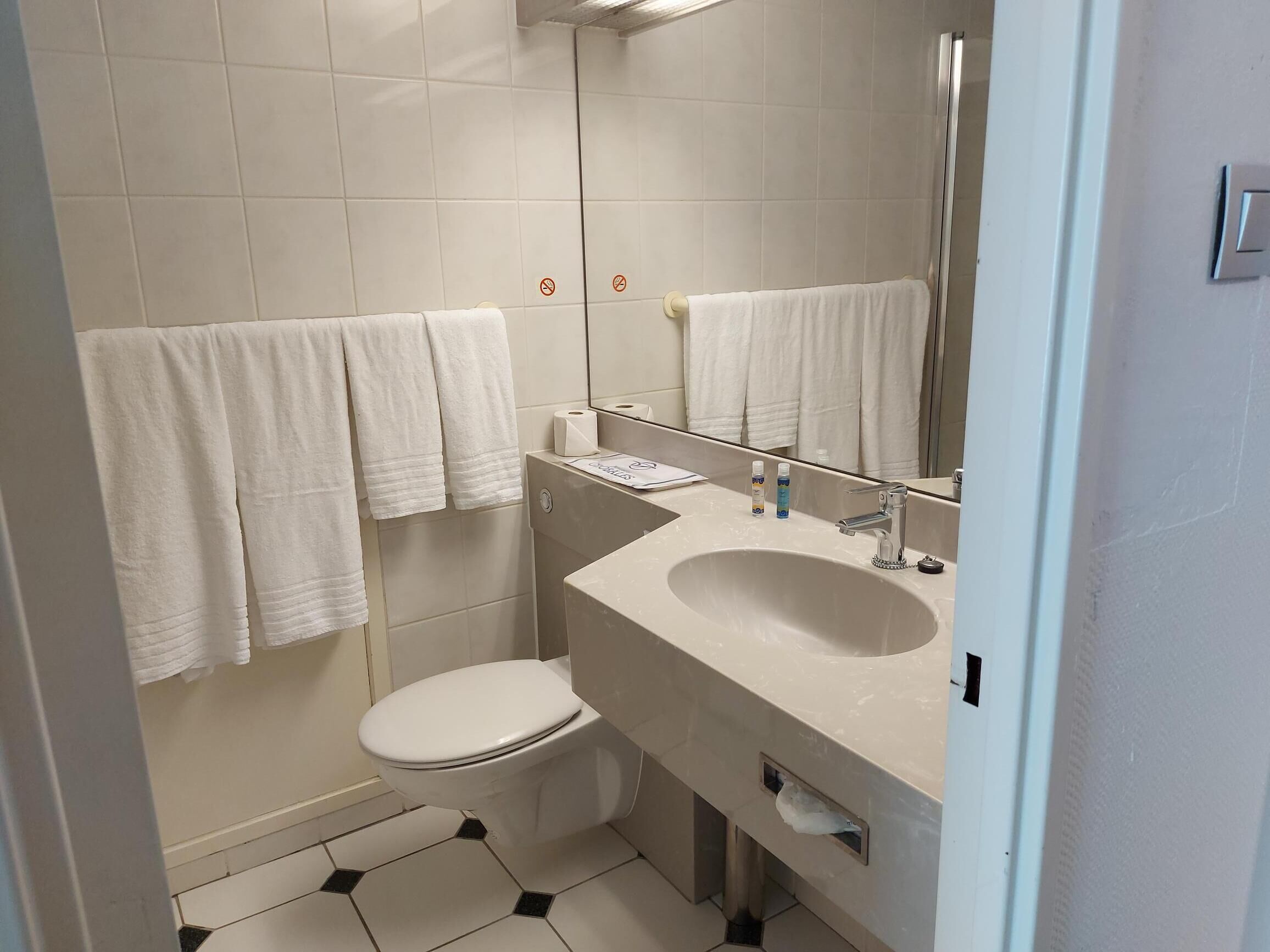 A bathroom with a toilet, sink, and mirror. There are white towels hanging on the wall.