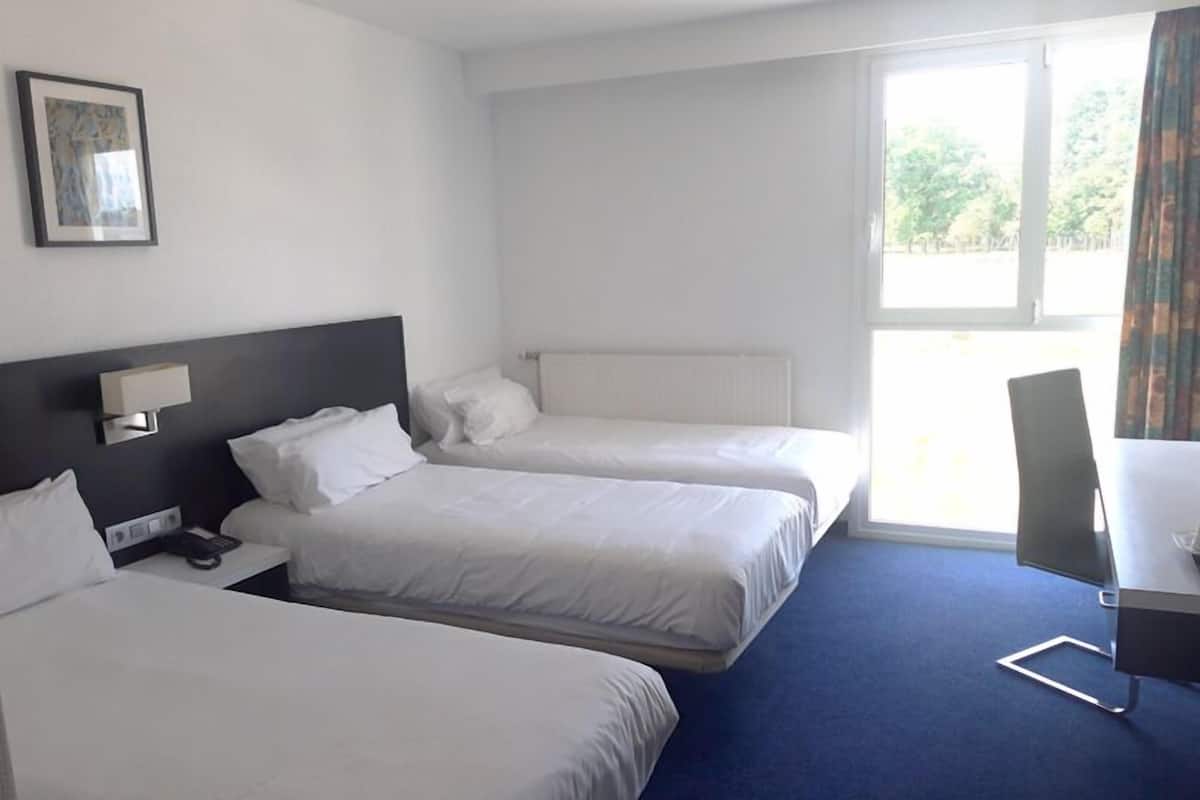 Ein Hotelzimmer mit zwei Betten, einem Schreibtisch, einem Stuhl und einem Fenster mit Vorhängen.