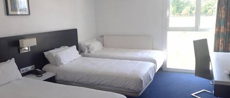 A hotel room with two beds, a desk, a chair, and a window with curtains.