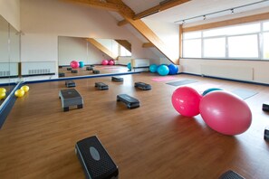 Ein geräumiger Fitnessraum mit Holzböden, Trainingsgeräten und großen Fenstern.