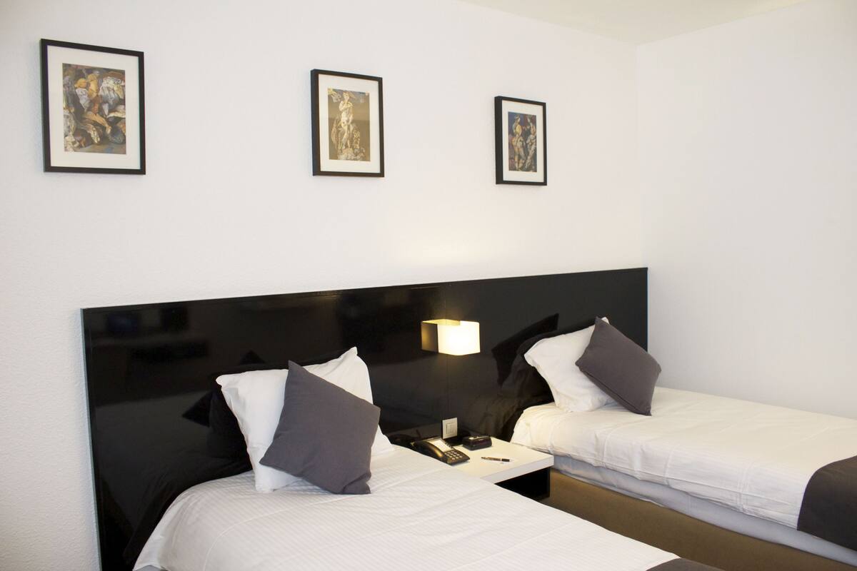 Ein Hotelzimmer mit zwei Betten, einem Nachttisch und gerahmten Kunstwerken an der Wand.