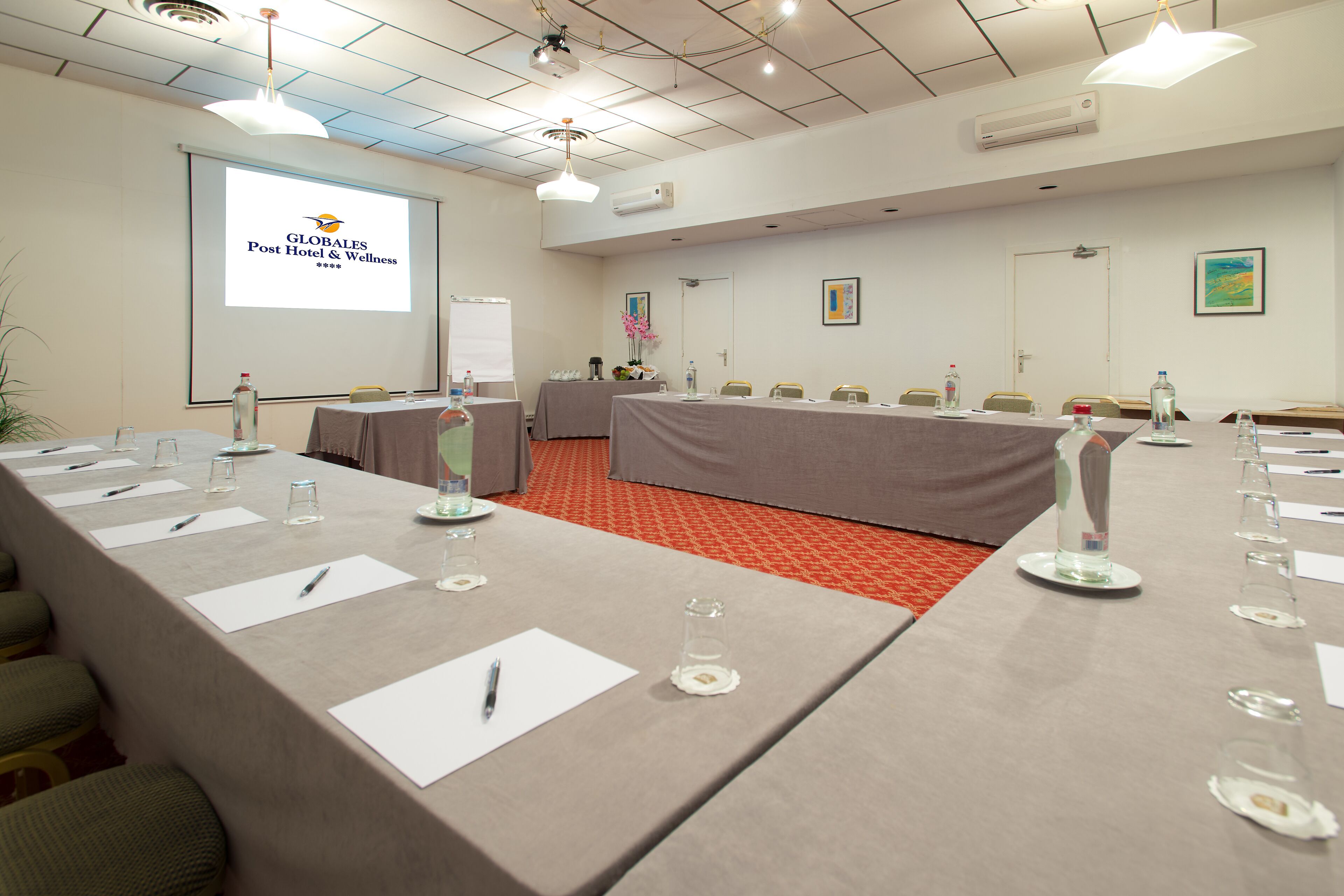 A conference room with a long table, chairs, a projector screen, and a carpeted floor.