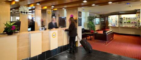 A hotel reception area with a reception desk, a clock, and a plant.