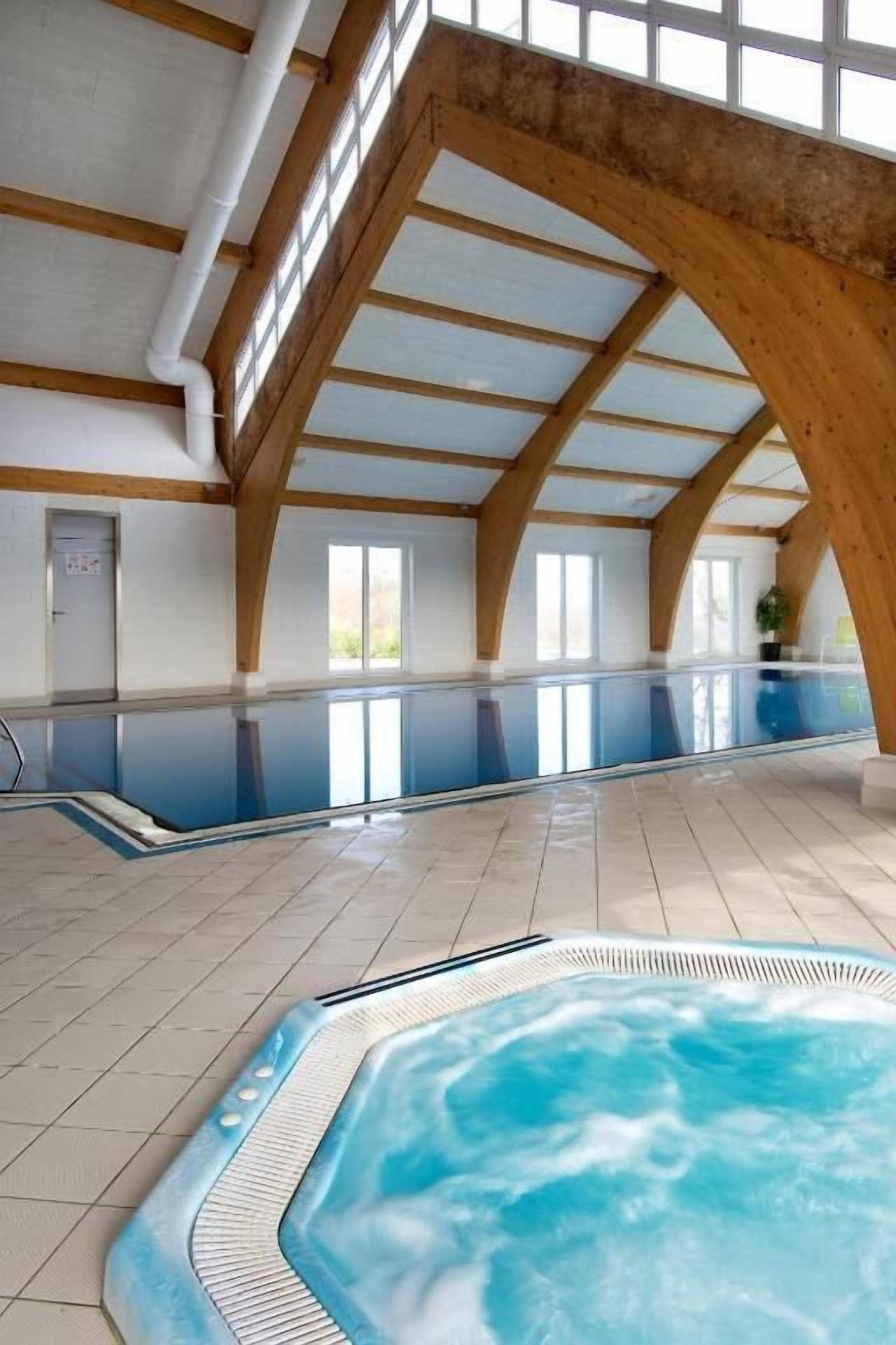 An indoor swimming pool with a hot tub, wooden beams, and large windows.