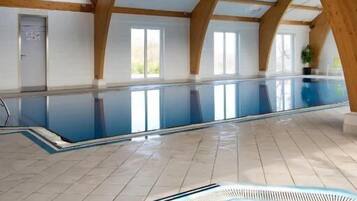 Una piscina interior con jacuzzi, vigas de madera y amplios ventanales.