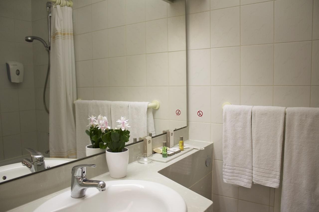A bathroom with a white sink, a mirror, a shower, and two towels hanging on the wall.