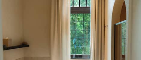 Un baño con bañera, una ventana con cortinas, un estante con artículos de aseo y un perchero para toallas.