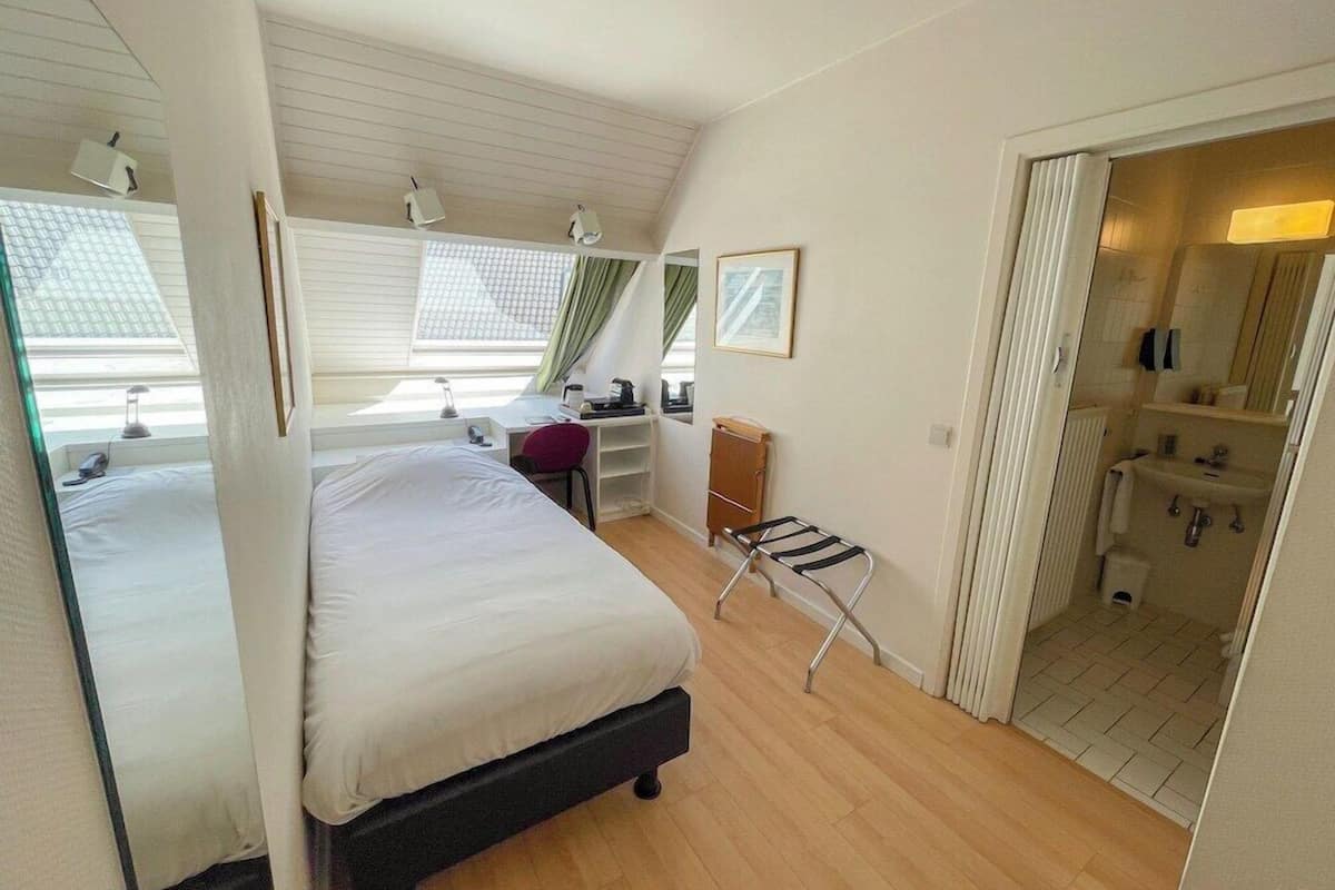 A bedroom with a bed, desk, chair, and a view of a bathroom.