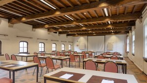 Un salón de conferencias con vigas de madera, mesas con sillas y ventanas amplias.