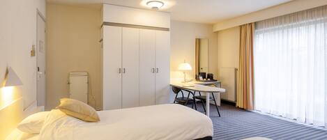 A hotel room with two beds, a desk, a chair, a lamp, a mirror, and a window with curtains.