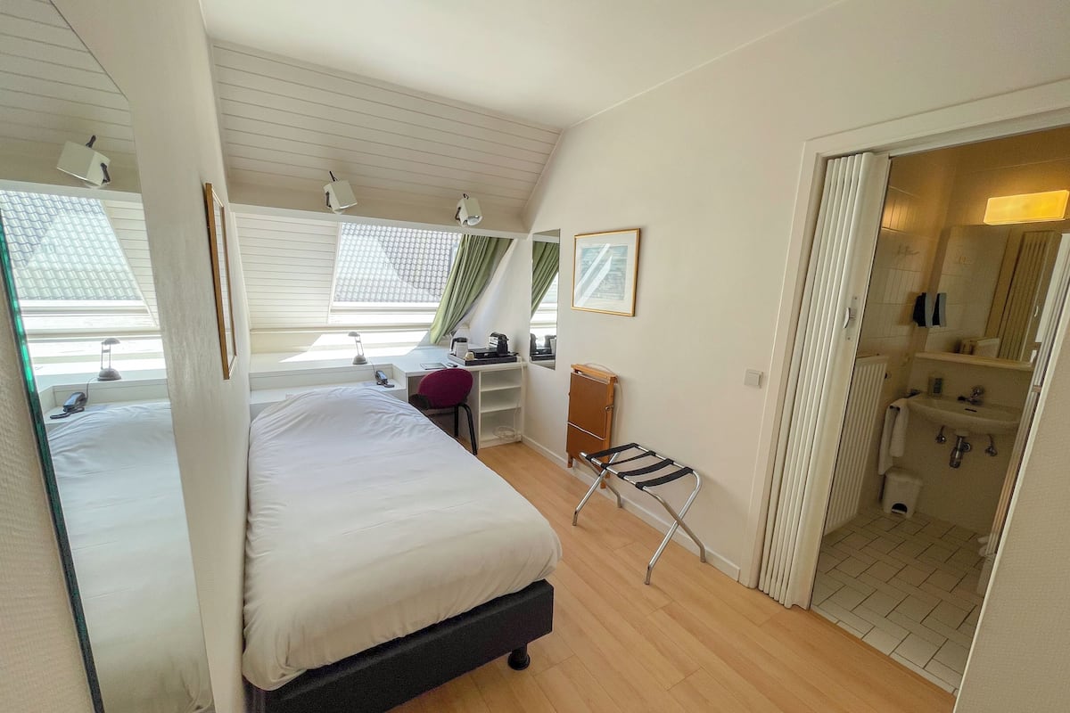 A bedroom with a bed, desk, chair, and a view of the bathroom.
