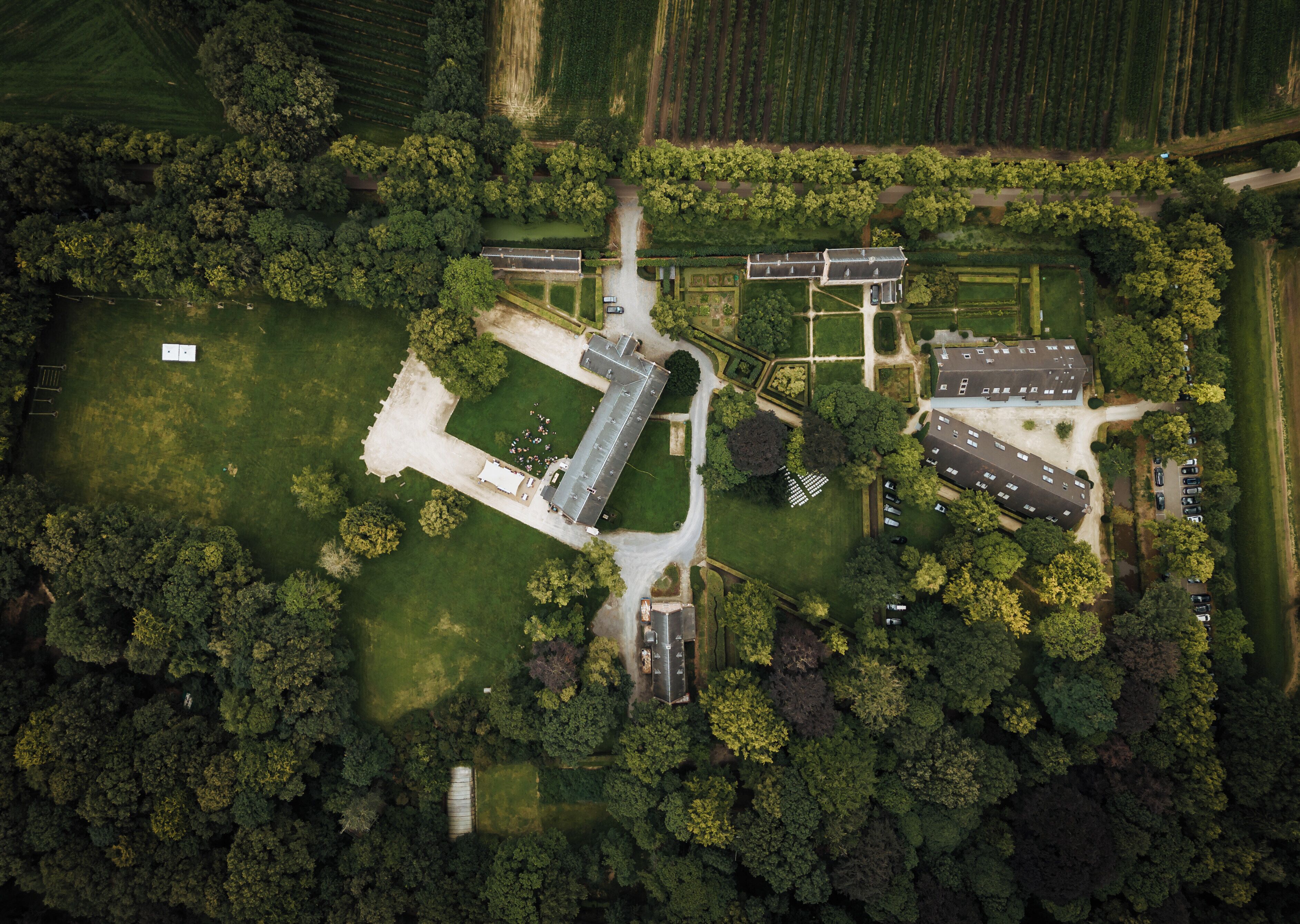 An aerial view of a property with a large central building, multiple parking areas, and surrounding greenery.