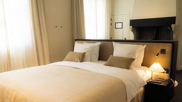 Une chambre d’hôtel avec un lit, une table de chevet avec une lampe, une cheminée et une porte.