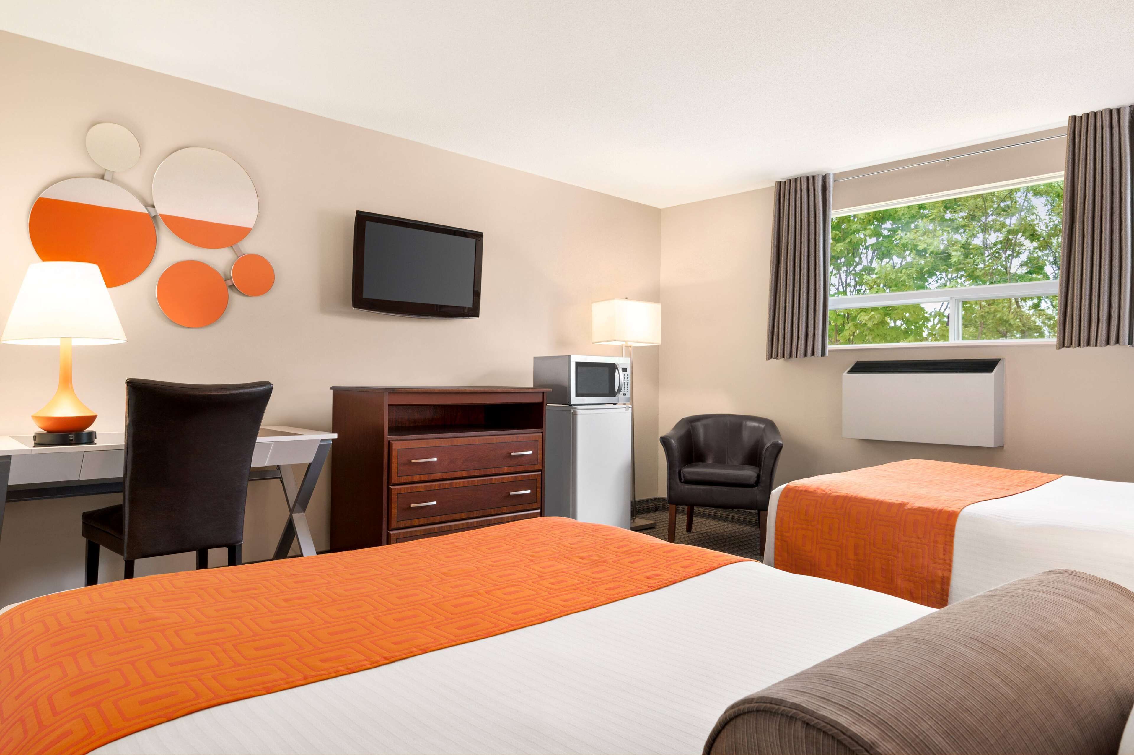 A hotel room with two beds, a desk with a computer, a television, a lamp, and a window with curtains.