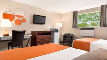Habitación de hotel con dos camas, un escritorio con computadora, televisor, lámpara y ventana con cortinas.