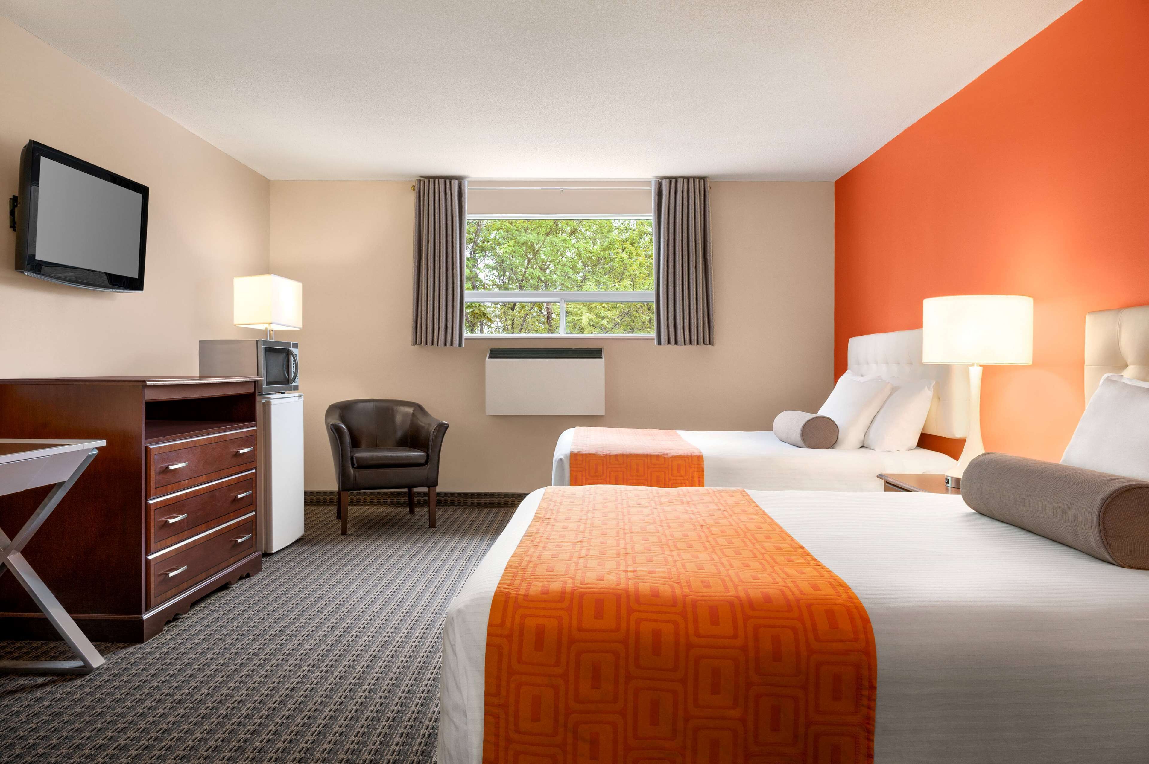 A hotel room with two beds, a desk, a chair, a TV, and a window with curtains.