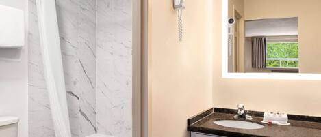 A bathroom with a shower, toilet, and sink with a mirror above.