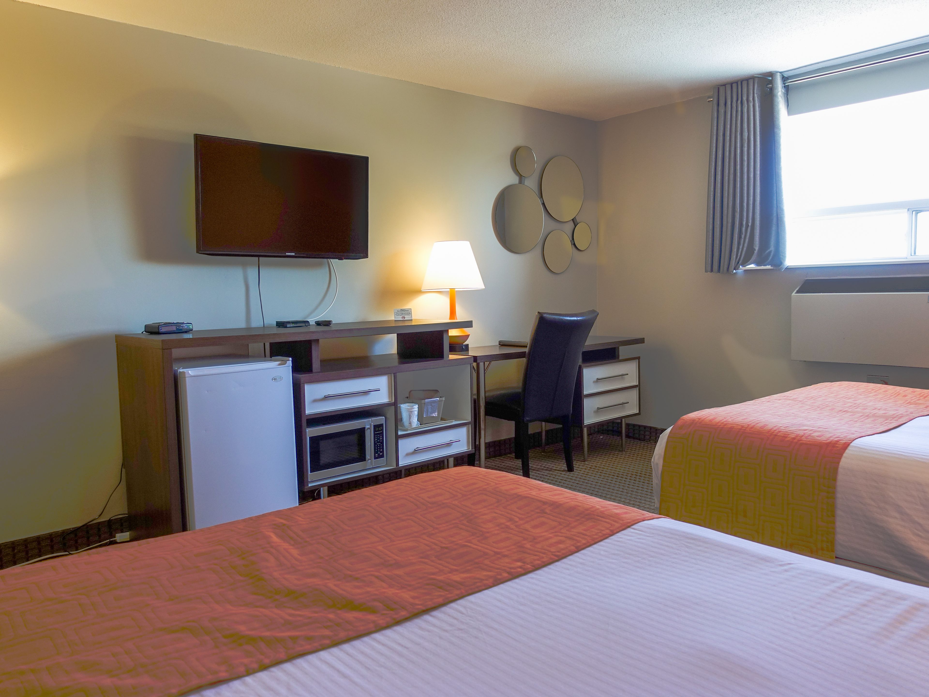 Habitación de hotel con dos camas, un escritorio con computadora, televisor y microondas.