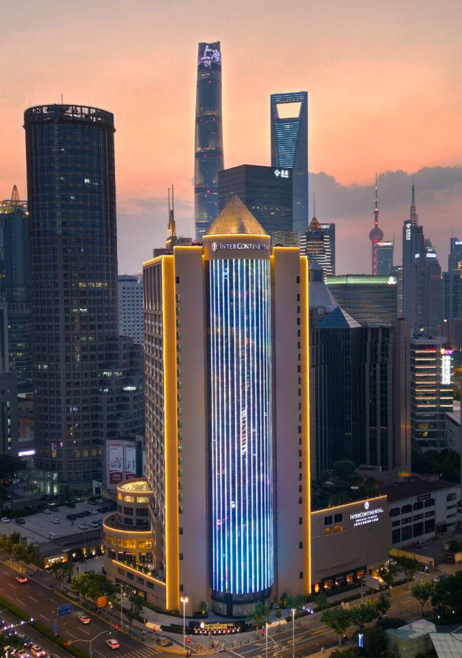 A high-rise building with a distinctive vertical light pattern, surrounded by other skyscrapers and a busy street.