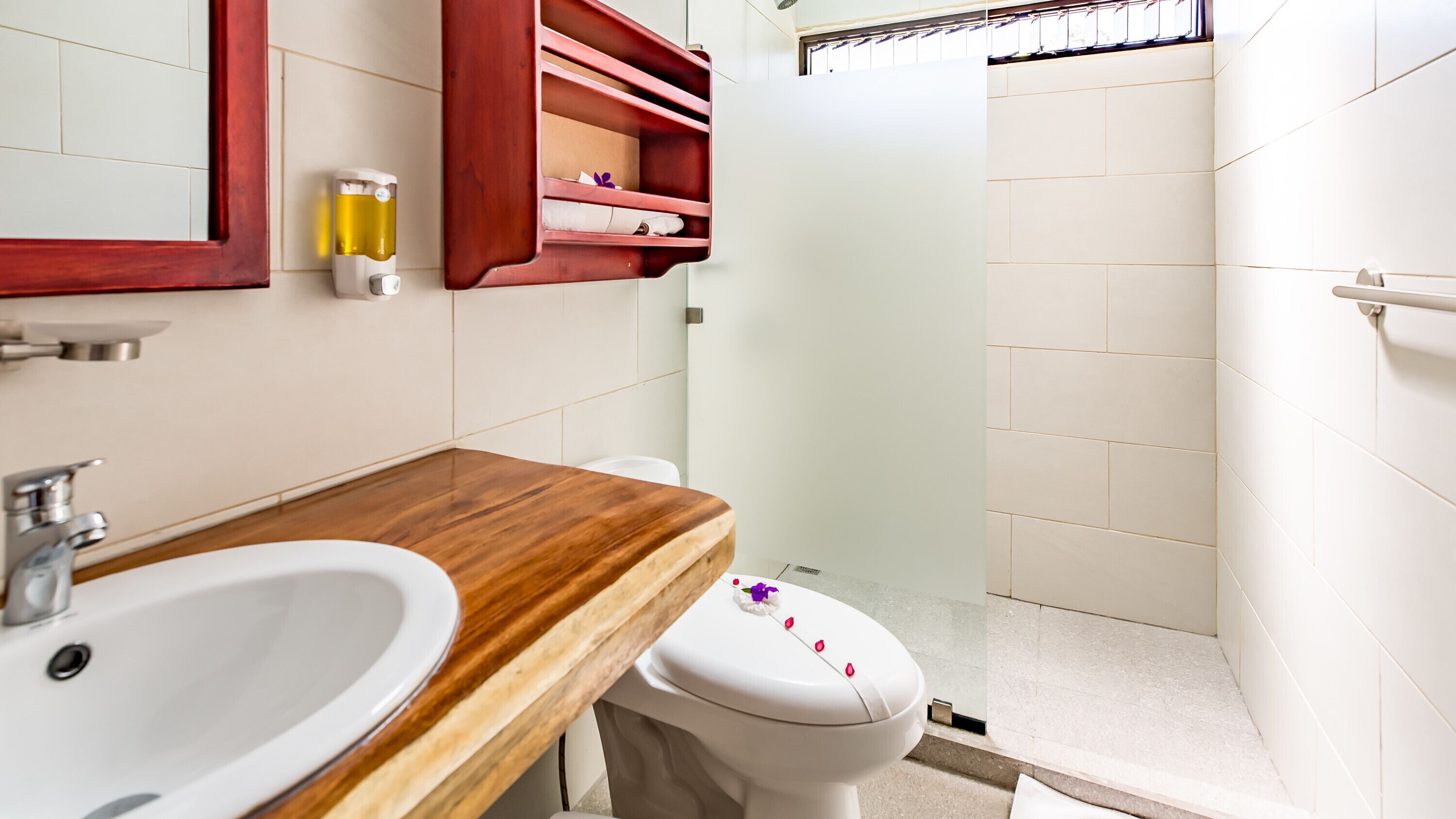 Ein Badezimmer mit einem Holz-Waschtisch, einem weißen Waschbecken, einer Toilette und einer Duschkabine aus Glas.