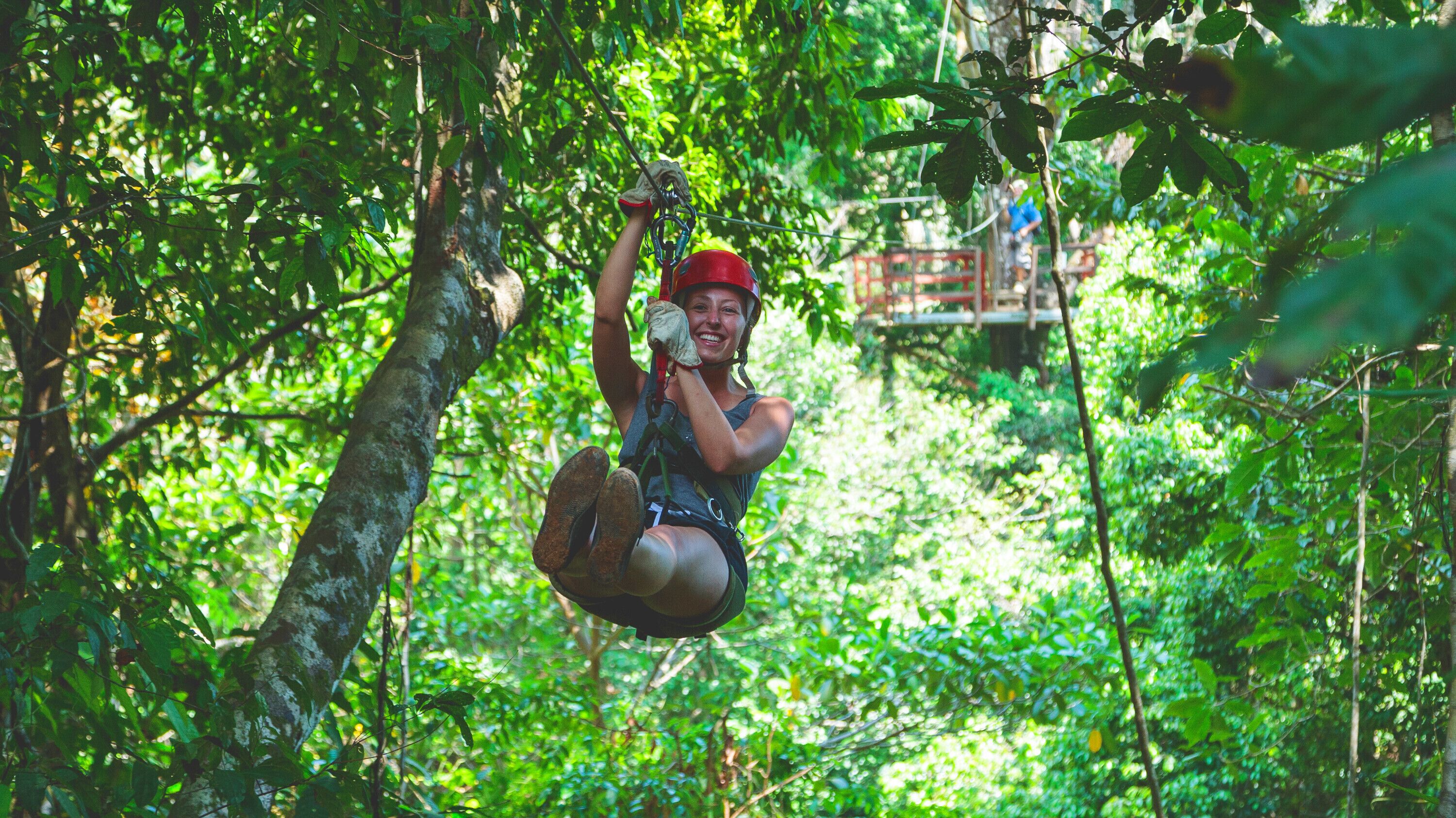 A person zip-lining through a dense forest with a safety harness and helmet.