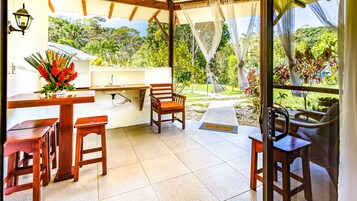 Un porche techado con un lavabo, sillas de madera y una mesa.