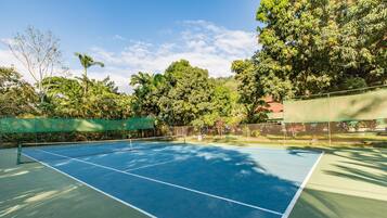 Un campo da tennis all'aperto con rete, circondato da alberi e una recinzione.
