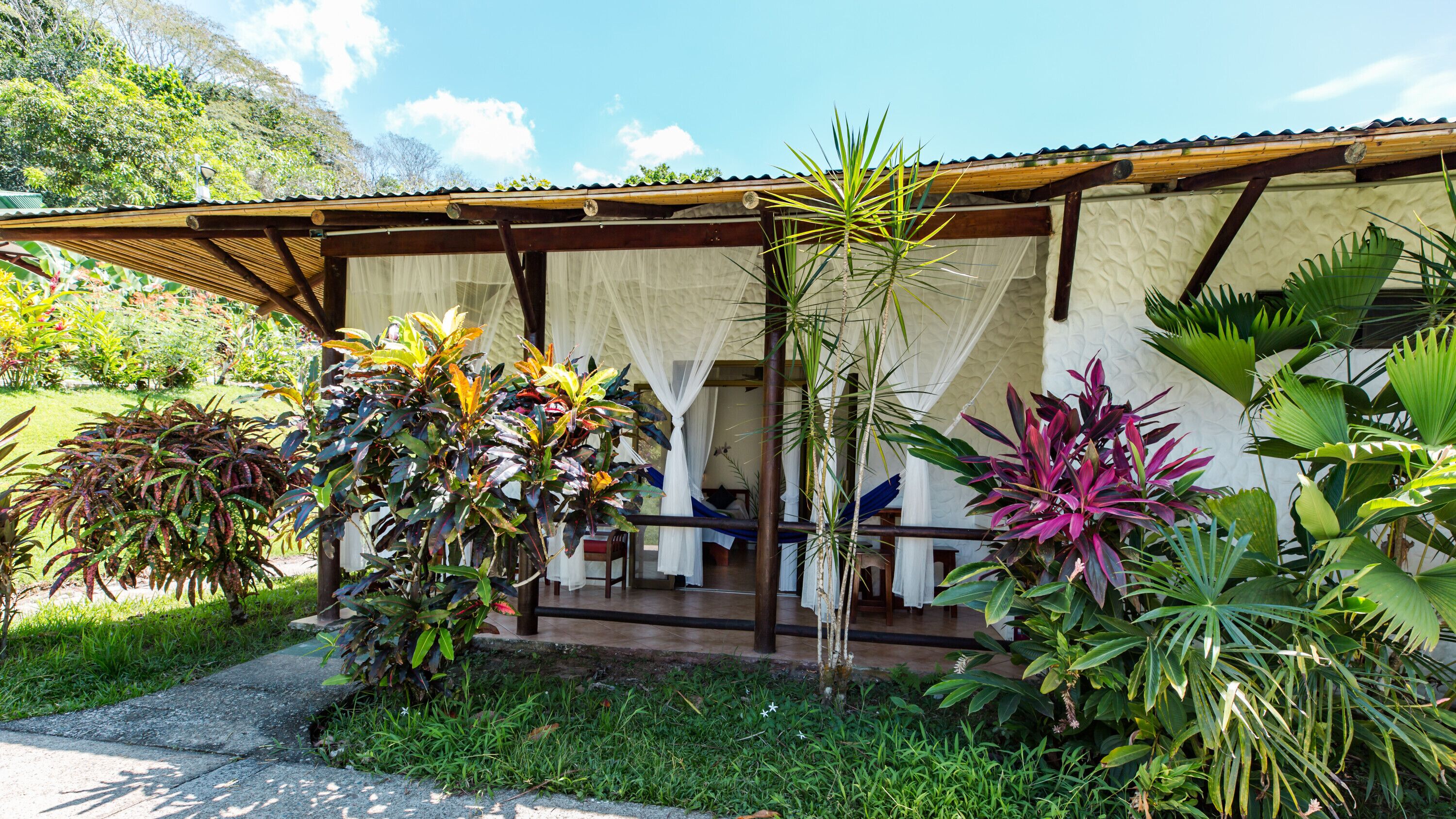 A bungalow with a covered porch, surrounded by lush tropical plants.