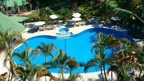 Une grande piscine d’un bleu éclatant, entourée de palmiers et de chaises longues.