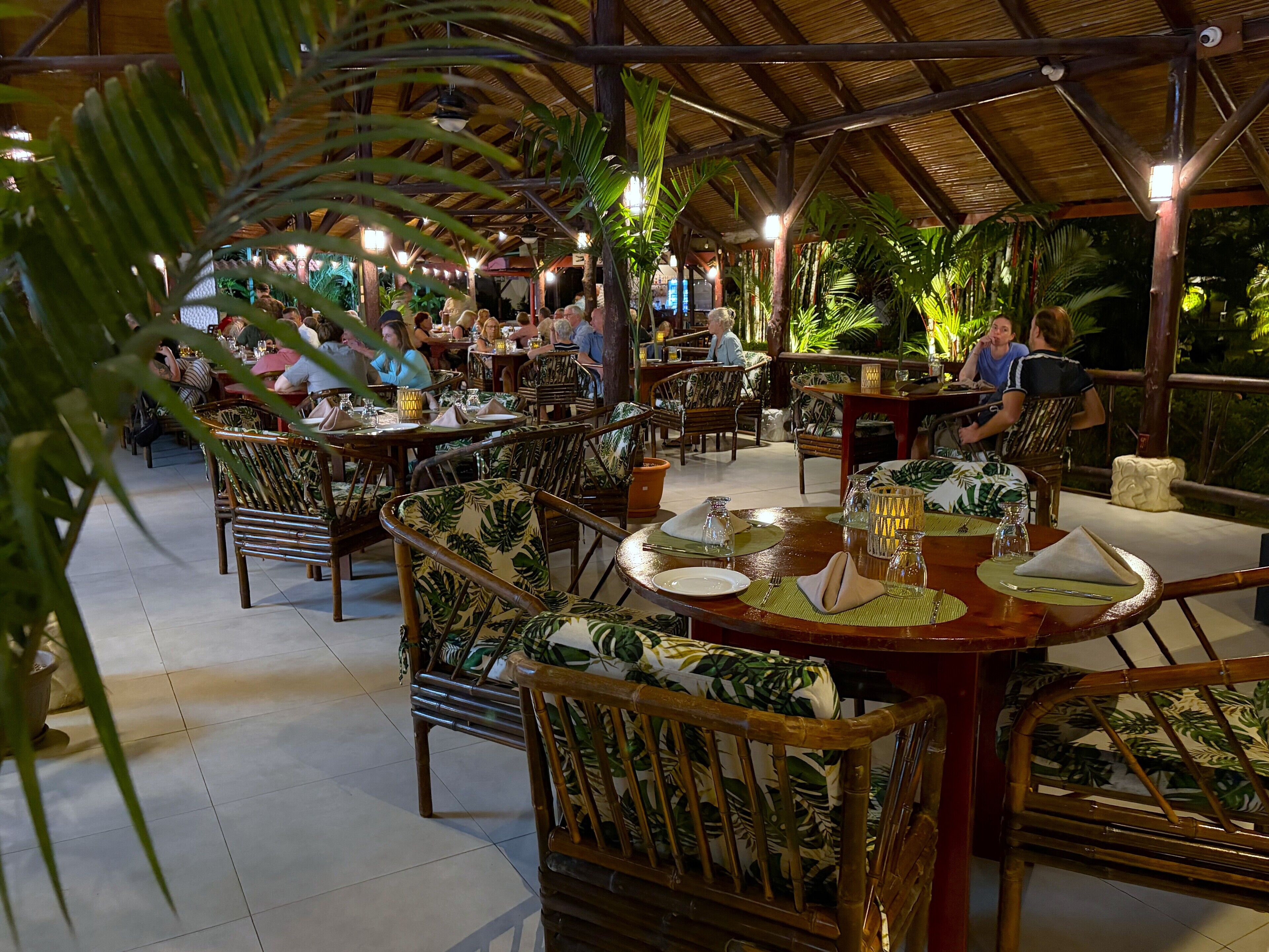 Un restaurant intérieur avec des tables et des chaises en bois, entouré de plantes tropicales.