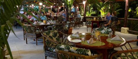 Un restaurant intérieur avec des tables et des chaises en bois, entouré de plantes tropicales.