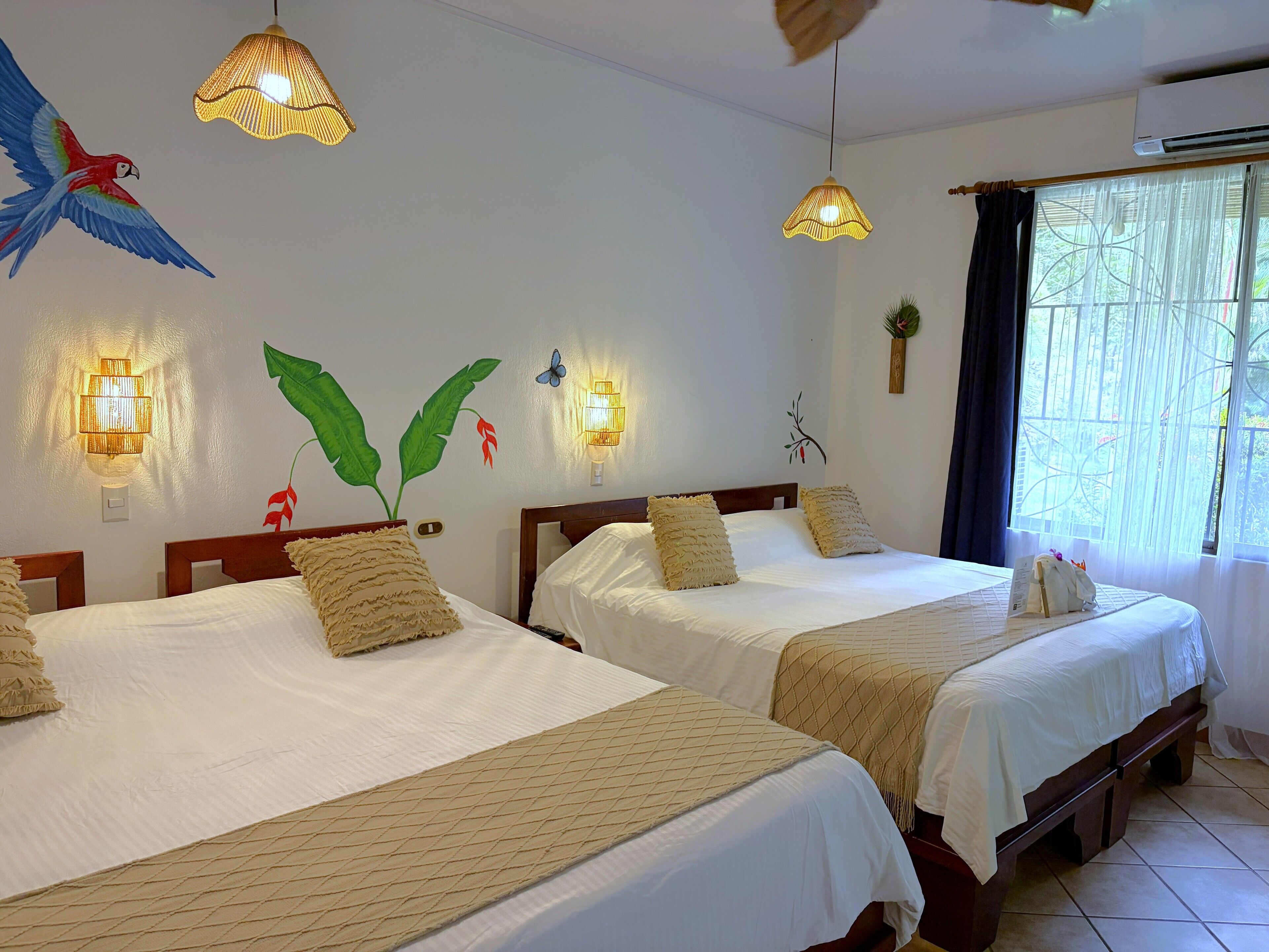A hotel room with two beds, each with a wooden headboard and white bedding. There are wall-mounted light fixtures and a window with curtains.