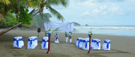 Decoração de casamento na praia com cores branco e azul, um dossel branco e arranjos florais.