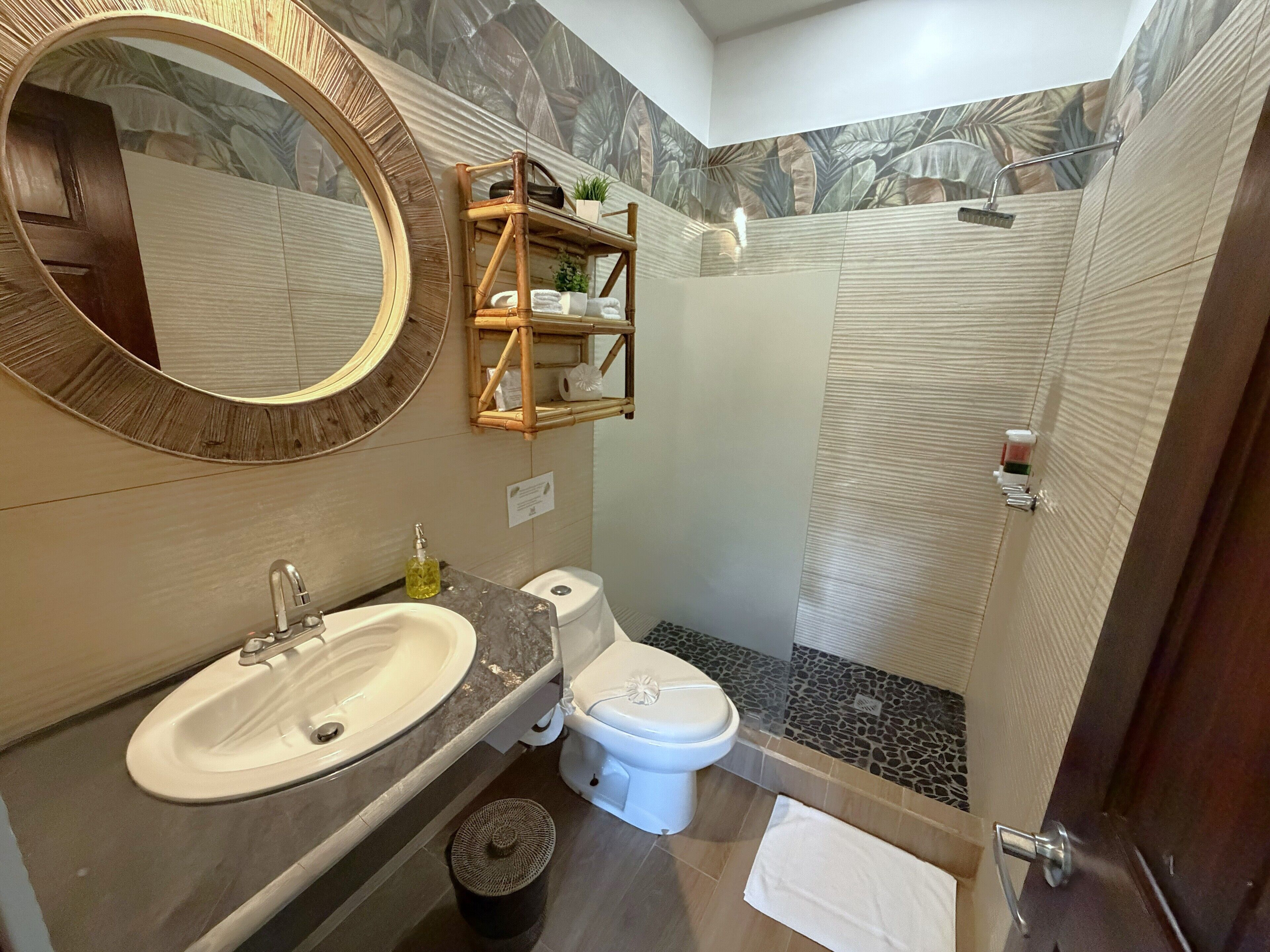 Ein Badezimmer mit rundem Spiegel, Waschbecken, Toilette, Dusche und Ablage für Toilettenartikel.