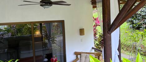A room with a ceiling fan, a sliding glass door leading to a garden, a wooden bench, and a table with chairs.