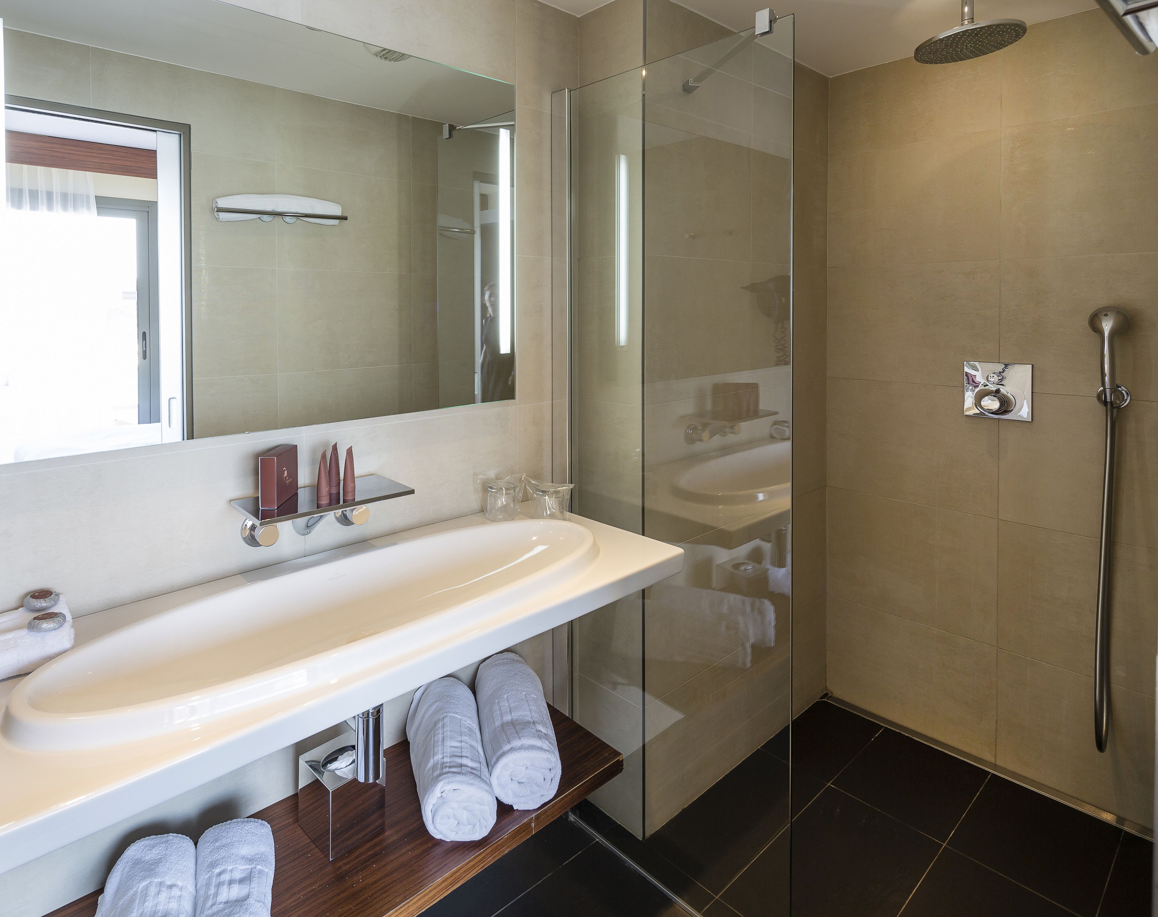 Un baño moderno con ducha de vidrio, lavamanos blanco y espejo sobre él.