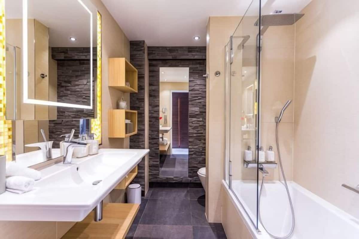 A modern bathroom with a glass shower enclosure, a double sink vanity, and a stone accent wall.