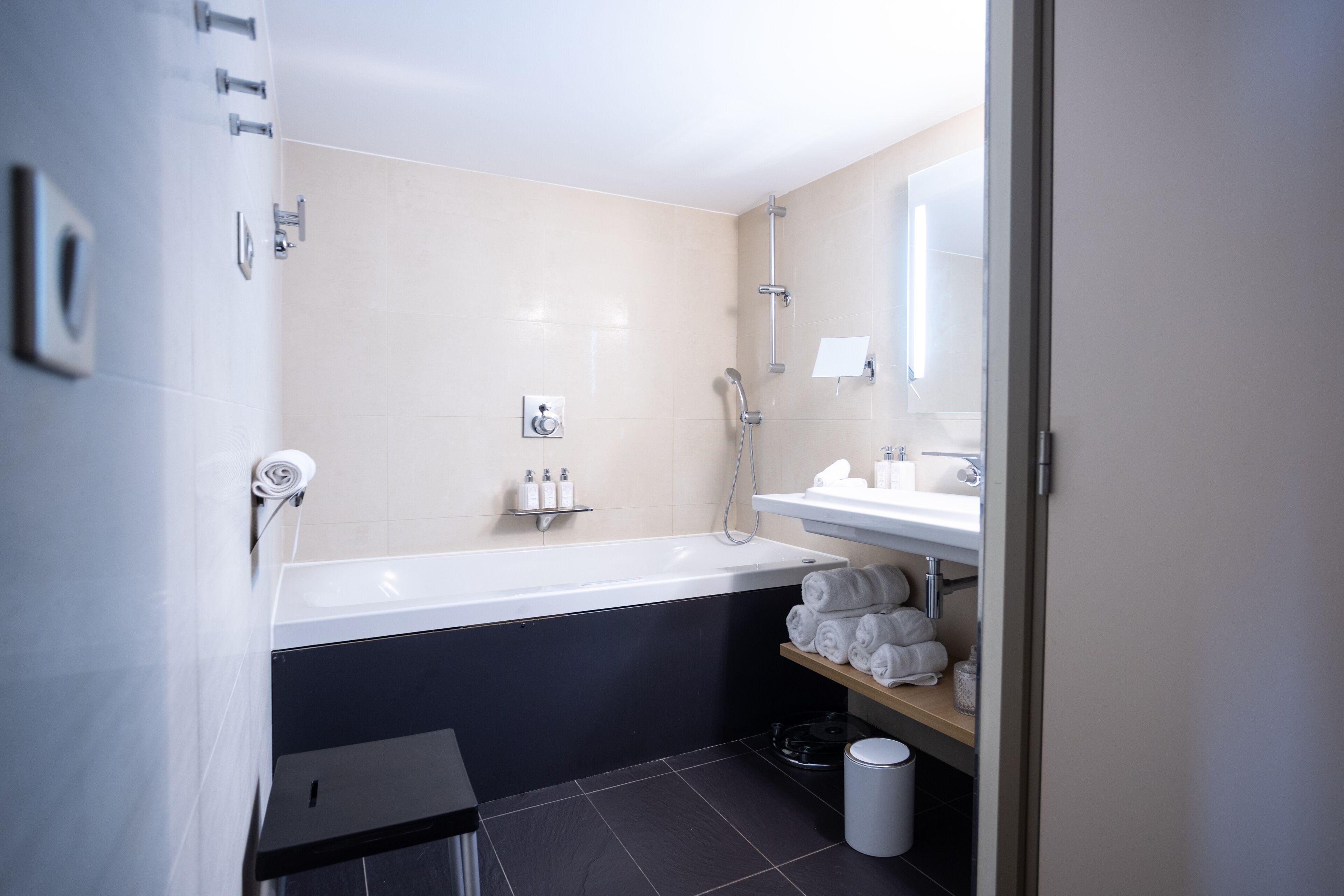 A modern bathroom with a bathtub, a shower, a sink, and a toilet. There are towels and toiletries on the shelves.